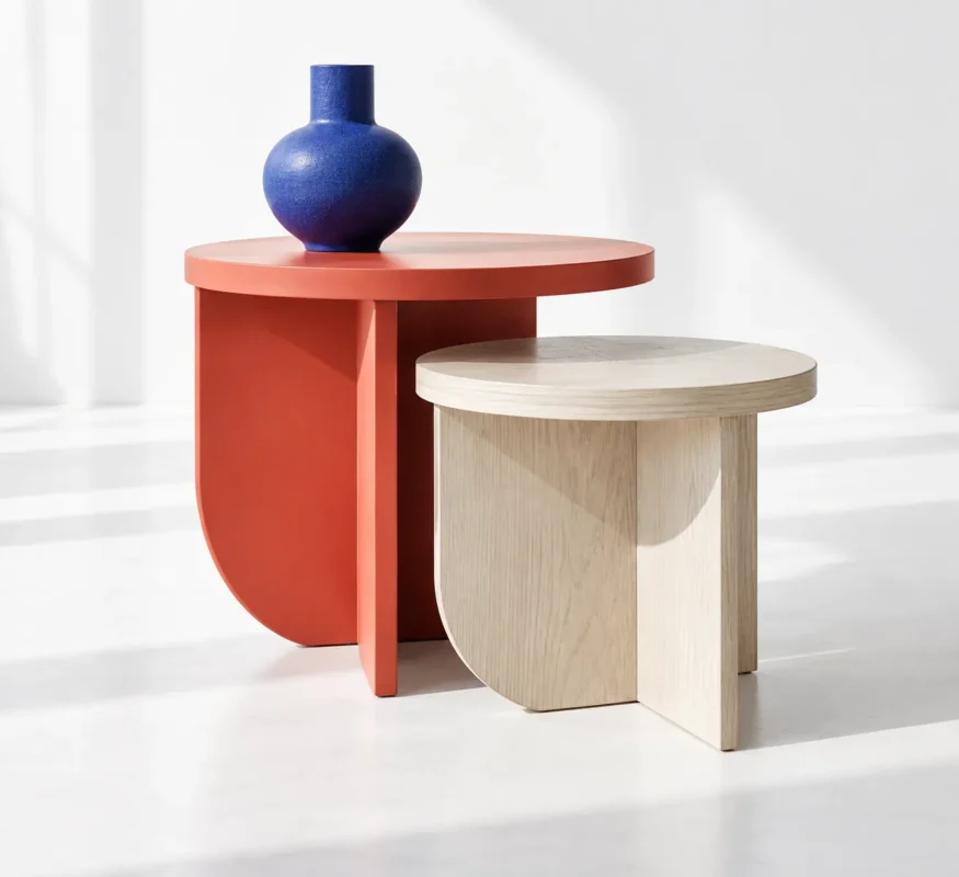 Coral-red and pale-wood sculptural tables with a cobalt vase in a bright white studio